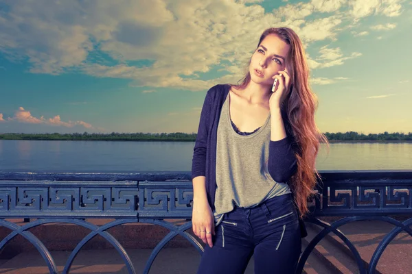 Nadenkend vrouw luisteren naar de mobiele telefoon voor waterkant hek — Stockfoto