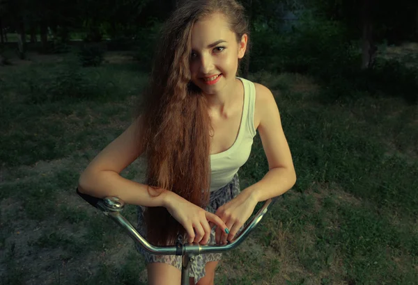 Chica feliz en bicicleta sonriendo en el campo mirando a la cámara —  Fotos de Stock