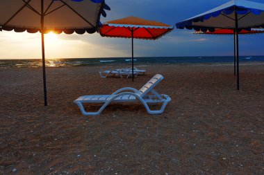 Plaj şezlong ve şemsiyeler günbatımı denizde ıssız sahil üzerinde.