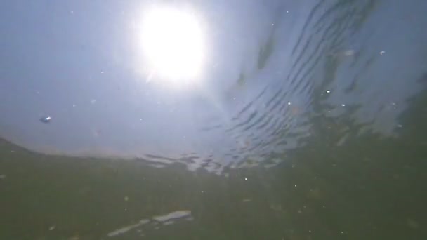 Подводный кадр с обломками снарядов, плавающих вокруг, и солнце, сияющее в воде — стоковое видео