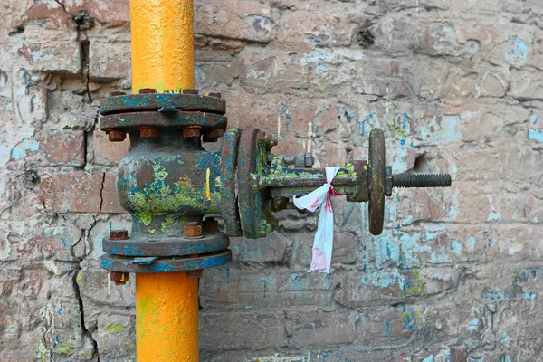 Alte Gasleitung in gelbem Rohr lackiert und rostiges Ventil mit veralteten Farbflecken an der Ziegelwand — Stockfoto