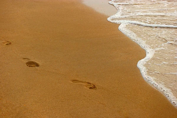 Sandy beach, våg och fotspår bakgrundsbelyst i solnedgång — Stockfoto