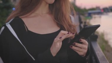 Şehirdeki nehir kıyısında güzel bir kız tabletle çalışıyor.