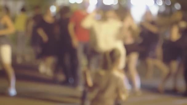 Crowd are dancing latina social dances in the street and there is little funny girl on foreground trying to imitate, defocused real-time shot. — Stock Video