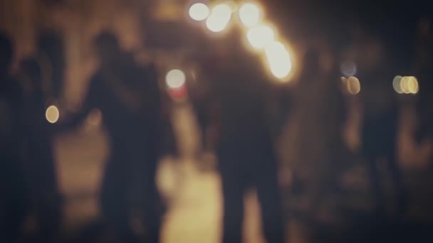 Defocused silhouettes of dancing couples in the night street in slow motion.