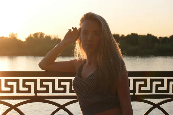 Undisturbed blond haired lady posing leaning at fence by hand in sunset light full of lovesikness — ストック写真