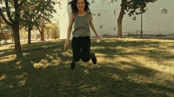 Chica saltando sobre hierba verde con botella de agua en la mano — Vídeos de Stock