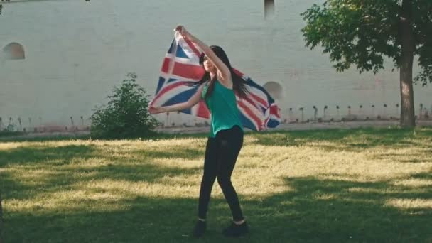 Молодая женщина танцует с Юнион Джек в ее руках в летний день — стоковое видео
