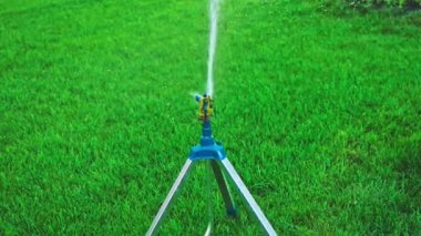 Tripod fıskiyeleri çimlerin üzerinde duruyor ve etrafa su saçıyor.