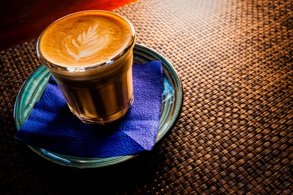 Flat white coffee is served on saucer over the table with bamboo mat backlit, copyspace