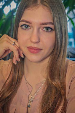 Sarışın genç bayanın sakin bir yüz ifadesi. O, elleriyle çenesine dokunuyor ve sakince kameraya bakıyor..