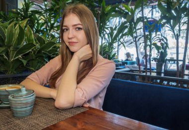 Kafeteryada uzun koyu sarı saçlı hoş bir bayanın yan görüntüsü. Yalnızlıkta kahve içen kadın görüntüsü