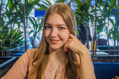 Kafede, çenesine elle dokunurken kahkaha atan genç ve güzel bir bayan resmi..