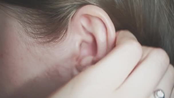 Вухо леді крупним планом. Дама грає зі своїм світлим волоссям над її вухом — стокове відео