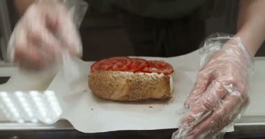 Şeffaf eldivenli bir kadın yerel fast food 'ta sandviç hazırlıyor. Açık çöreğe taze sebze ekliyorum..