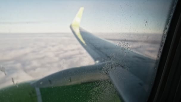 Вид на крило літака і хмарне покриття через вікно з невеликими краплями води і деякими брудами — стокове відео