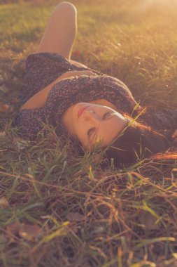 Nice lady dark-haired lying in autumnal grass, backlit by setting sun, copyspace on foreground
