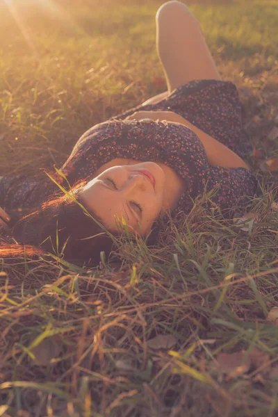 Gülümseyen koyu renk saçlı bir kadının portresi Sonbahar çimlerinde uzanmış sarı ışıklı arka ışıklandırmayla