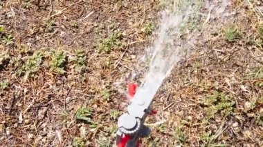 Irrigation system sprays water on the drying grass which is fed to it by green hose, slow motion from above