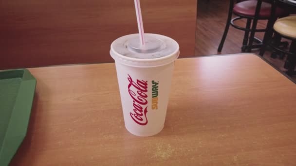 Astrakhan, Russia, 26 June 2021: Paper cup with red-white straw in co-branded with Coca-Cola and Subway set on table zoom-in shot — Vídeo de stock