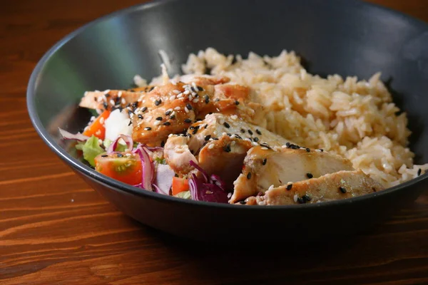 Tasty curry indian food - bowl of spicy stir rice with chicken and vegetables on wooden table