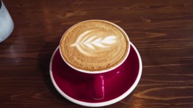 Man add a brown sugar cube into the hot latte coffee with froth art on top of milk froth slomo