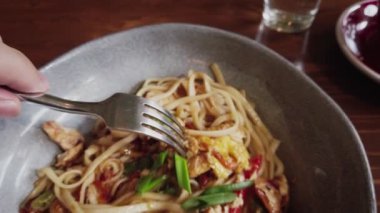 Udon pasta japanese noodles bowl fried vegetables, egg and chicken breast, man winding the noodles with fork