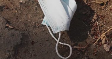 Dirty surgical medical mask with ear straps thround at the ground. Typical 3-ply doctor mask to cover the mouth and nose. Used procedure mask from bacteria. Ecology waste concept