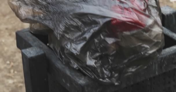 Cubo de basura de la ciudad lleno de basura con bolsa de basura negra revoloteando en el viento — Vídeos de Stock