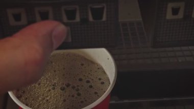 Makineyi kullanarak meşrubat kola bardağına dökerek.