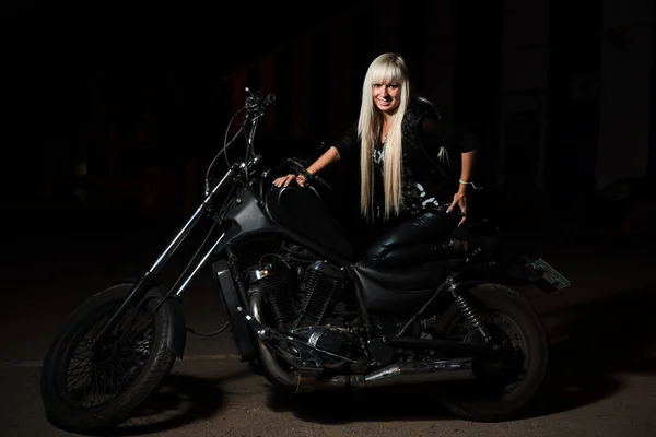 Sexy Biker Mädchen posiert auf Motorrad in der Nacht. Sie blickt zufrieden in die Kamera — Stockfoto
