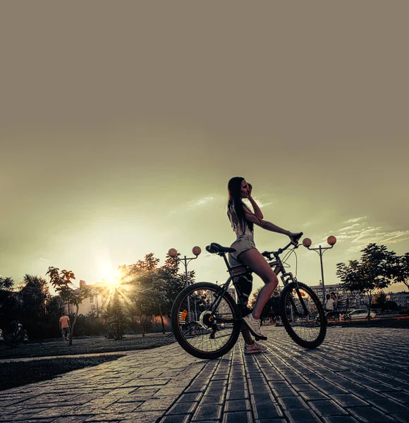 骑自行车的夜晚 迷人的身材苗条的女孩坐在城市小巷的自行车上 回头看 天空中的复制空间 — 图库照片