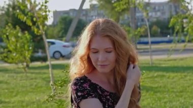 Gülümseyen mutlu kızıl saçlı, rüzgarda savrulan saçlarıyla parkta.
