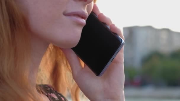 Jollyful dame aux cheveux rouges parlant par smartphone à l'extérieur, détail du menton et des lèvres — Video