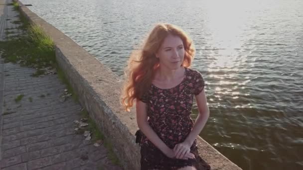 20s dame rousse est assis sur du béton. parapet côté rivière, elle a l'air réfléchie et préoccupée. Mouvement lent — Video