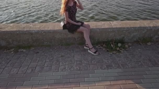 Move in shot focused at slim legs on young red haired lady sitting aside the pond — Stock Video