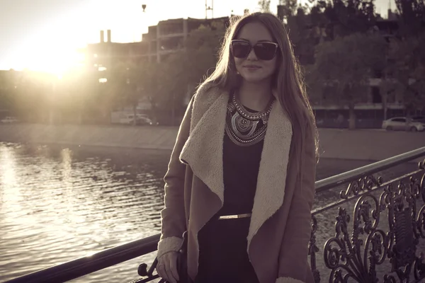 Sepia getöntes Retro-Porträt eines schönen Mädchens mit Sonnenbrille im Gegenlicht gegen Wasser, Instagram-Stil — Stockfoto