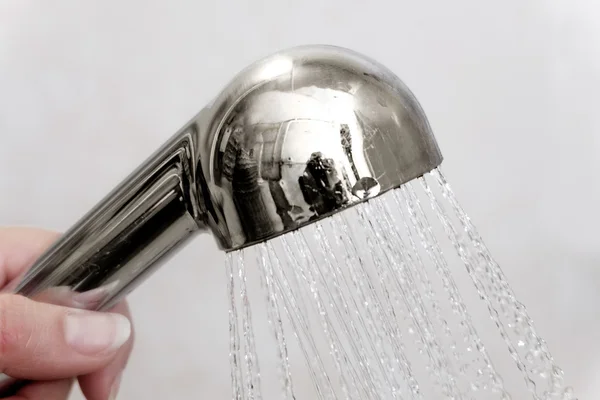 Cabeça de chuveiro cromada na mão com água derramando em gotas — Fotografia de Stock