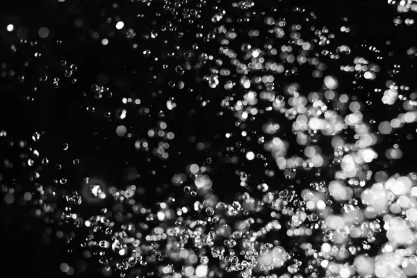Wassertropfen und verschwommener Lichtfleck schweben in der Luft auf schwarzem Hintergrund — Stockfoto