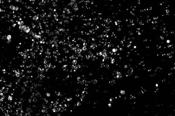 Wasser plätschert dahin. Tropfen transparenter Flüssigkeit fliegen auf schwarzem Hintergrund. — Stockfoto