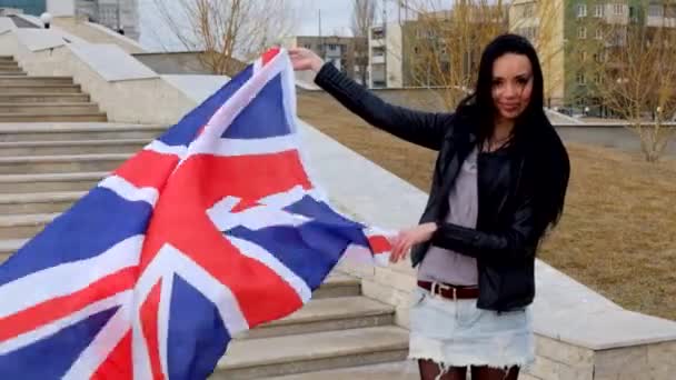 Sonriente latina morena sosteniendo la bandera de Union Jack ondeando por el viento — Vídeos de Stock