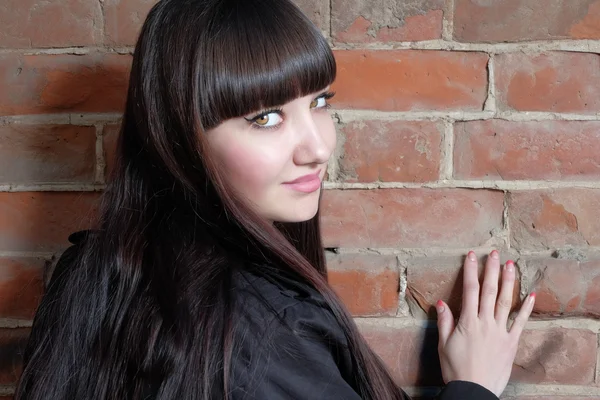 Mujer joven con el pelo castaño largo mira atrás espacio de copia en la pared de ladrillo rojo — Foto de Stock