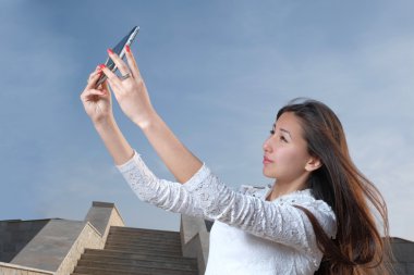 Casual Japon kadın uzun saçlı selfie şehir Park karşı adımları yapmak ve mavi gökyüzü ışık haze, boşaltmak temizlemek