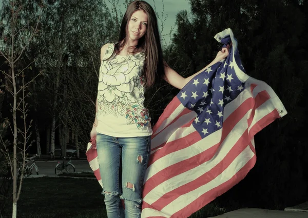 Joven morena hembra con una bandera americana en el parque tonificado instagram color — Foto de Stock