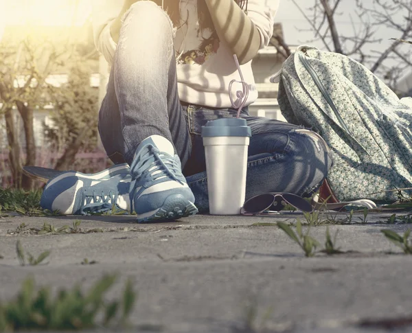 Joven chica de moda sentada en el suelo con una taza para llevar. Copyspace sobre asfalto — Foto de Stock