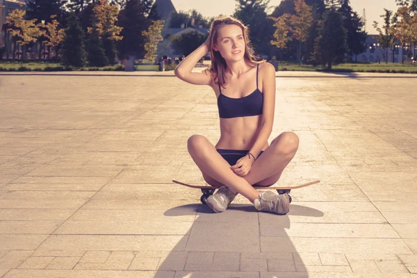 Sportieve vrouwen zitten op skateboard met haar benen gekruist — Stockfoto