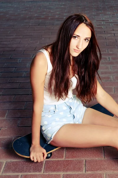 Young girl sitting on her skate board and looking at camera — Stock Photo, Image