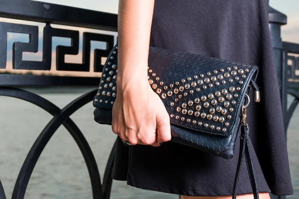 Jeune femme élégante à la mode avec sac à main noir pose à l'extérieur près de la clôture — Photo