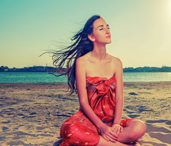Långhårig brunett meditera på sandstranden med smickrande hår flyga med vinden — Stockfoto