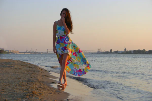 Jovem mulher em um vestido colorido na costa do oceano — Fotografia de Stock